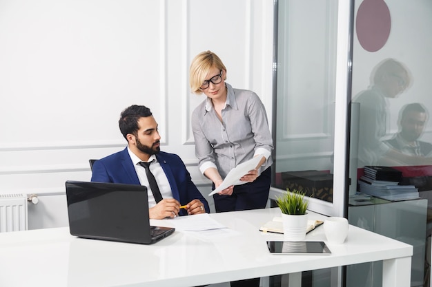 Patron barbu et femme blonde avec des documents à l'intérieur du bureau blanc