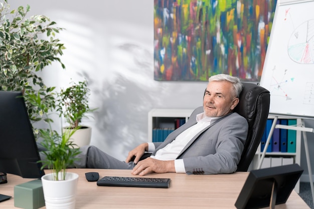 Un patron d'entreprise âgé souriant et détendu est assis dans une chaise confortable dans une position détendue avec les pieds