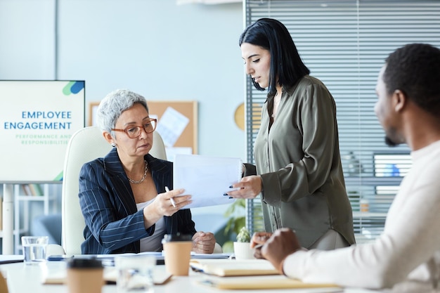 Patron féminin senior signant un document lors d'une réunion d'affaires avec l'équipe