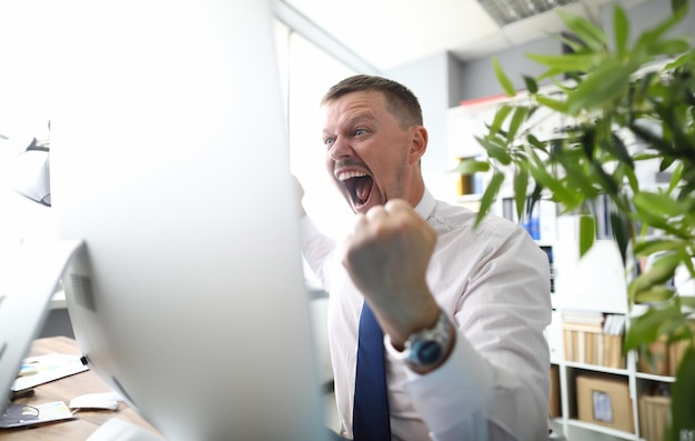 Un patron fou crie, menace d'un poing et regarde la caméra sur fond de bureau d'affaires