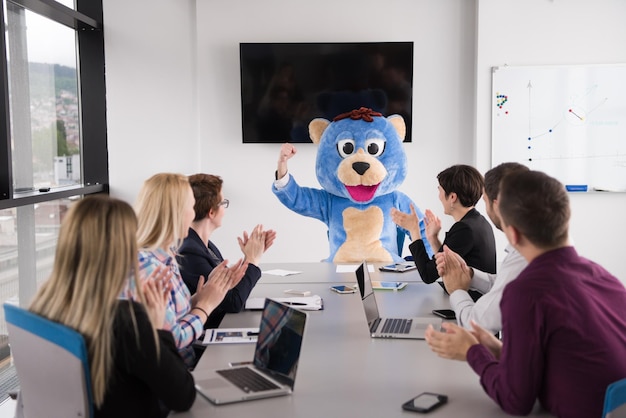 Patron habillé en ours en peluche s'amusant avec des gens d'affaires dans un siège social moderne