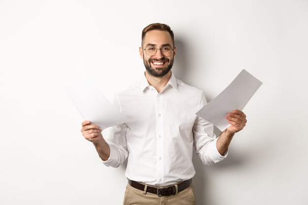 Patron satisfait souriant tout en tenant un bon rapport, lisant des documents, debout sur fond blanc.