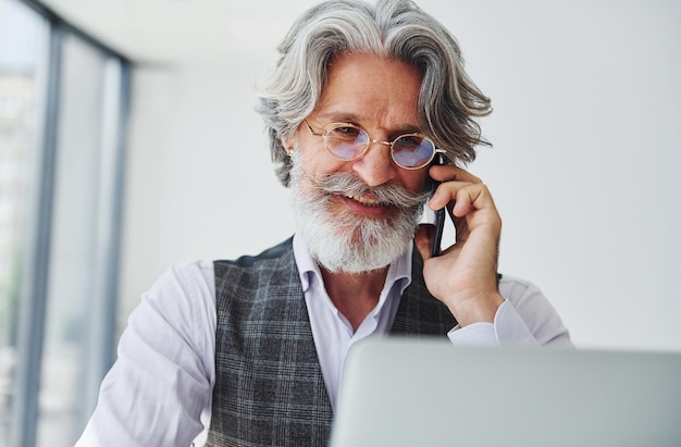 Patron en vêtements formels travaille au bureau Senior homme moderne et élégant aux cheveux gris et à la barbe à l'intérieur