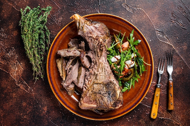 Épaule de chèvre ou d'agneau grillée dans une assiette rustique avec salade. Fond sombre. Vue de dessus.