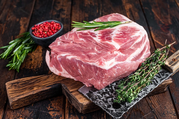 Épaule de porc viande crue pour steaks frais sur une planche à découper en bois avec couperet de boucher. Bois foncé