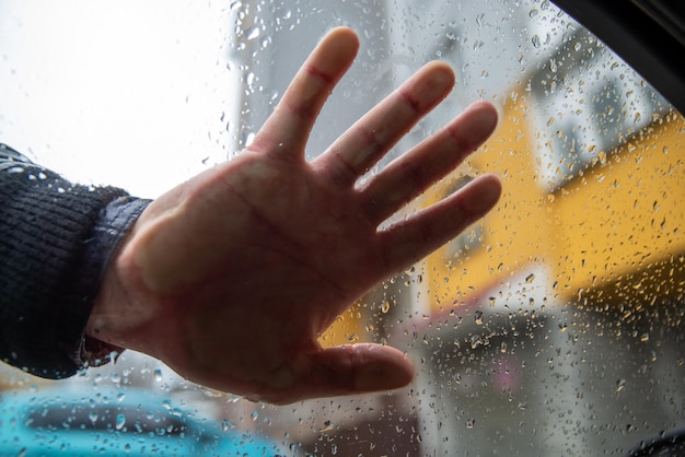 Paume de main d'homme sur le verre en gouttes de pluie