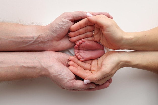 Photo les paumes du père la mère tiennent le pied du nouveau-né dans une couverture blanche les pieds du nouveau- né sur les paumes des parents photo macro studio des orteils, des talons et des pieds d'un enfant