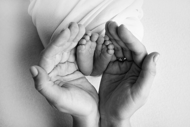 Les paumes du père la mère tiennent le pied du nouveau-né Pieds du nouveau-né sur les paumes des parents Photographie des orteils d'un enfant talons et pieds Photo en noir et blanc