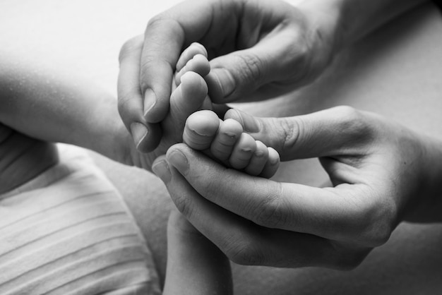 Les paumes du père, la mère tiennent le pied du nouveau-né. Pieds du nouveau-né sur les paumes des parents. Photographie en studio des orteils, des talons et des pieds d'un enfant. Noir et blanc.