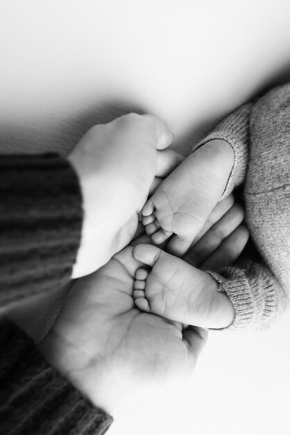 Photo les paumes du père la mère tiennent le pied du nouveau-né les pieds du nouveau- né sur les paumes des parents studio macro photo noir et blanc des orteils des enfants les talons et les pieds