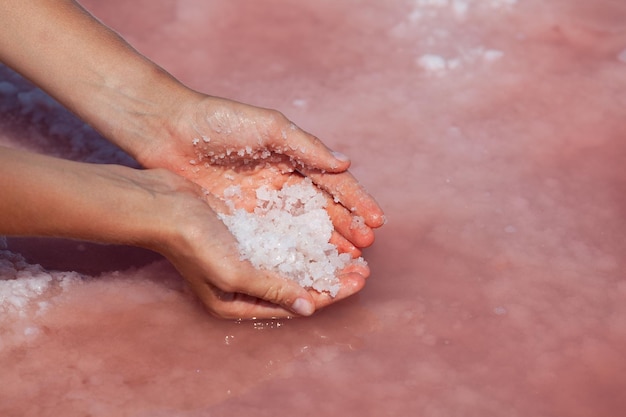 Les paumes des femmes recueillent le sel de guérison de la surface du lac rose Le sel rose est utilisé en cosmétologie