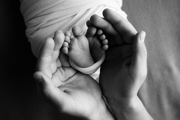 Les paumes des parents Un père et une mère tiennent un nouveau-né par les jambes Les pieds d'un nouveau-né dans les mains des parents Photo des talons et des doigts Macrophotographie en studio noir et blanc