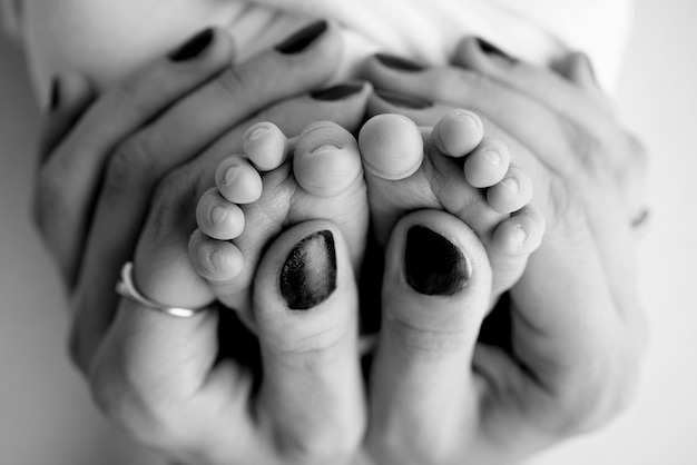 Les paumes des parents Un père et une mère tiennent un nouveau-né par les jambes Les pieds d'un nouveau-né dans les mains des parents Photo des talons et des doigts Macrophotographie en studio noir et blanc