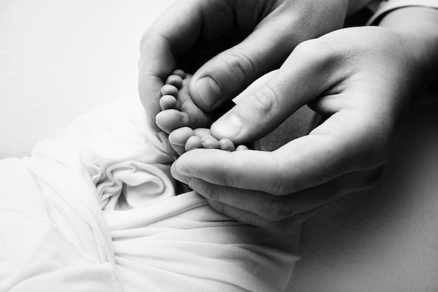 Les paumes des parents Un père et une mère tiennent un nouveau-né par les jambes Les pieds d'un nouveau-né dans les mains des parents Photo des talons et des doigts Macrophotographie en studio noir et blanc