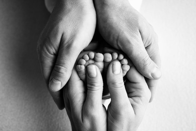 Les paumes des parents tiennent les pieds du nouveau-né Les jambes du nouveau-né sont entre les mains du père de la mère Photo macro des orteils des talons des pieds