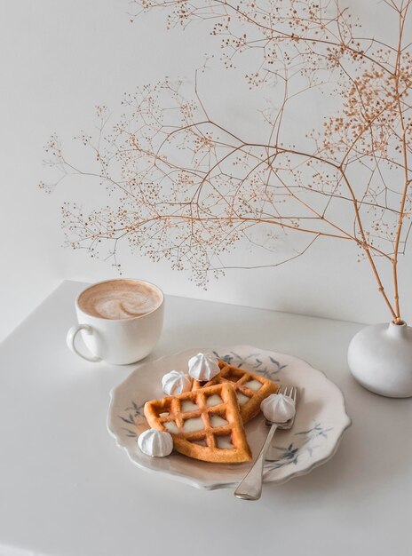 Une pause café confortable cappuccino et des gaufres avec du lait condensé et de la meringue sur un fond clair