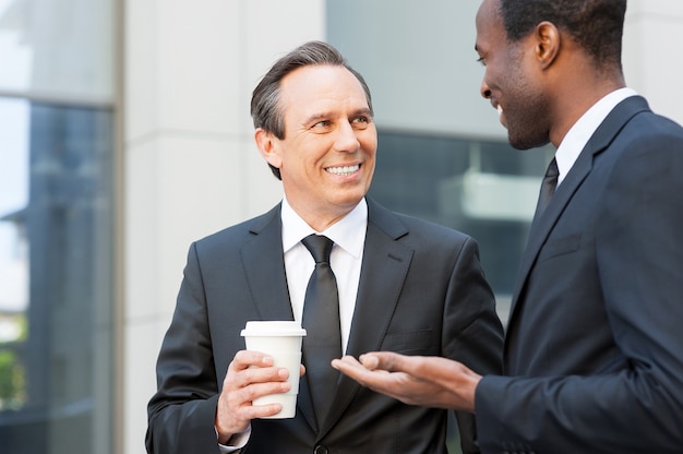 Photo pause café. deux hommes d'affaires joyeux qui parlent à l'extérieur tandis que l'un d'eux tient une tasse de café