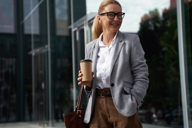 Pause-café élégante femme d'affaires heureuse portant des lunettes classiques tenant une tasse de café et