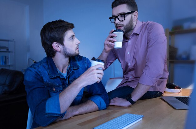 Pause café. Homme barbu agréable et attrayant, boire du café et se parler tout en faisant une pause du travail