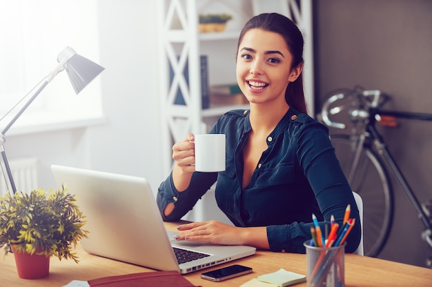 Pause café. Jolie jeune femme tenant une tasse de café et souriant