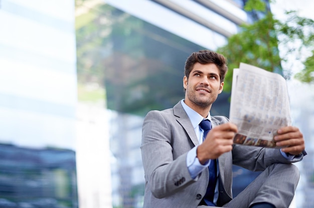 Une pause rapide pendant une journée bien remplie Un beau jeune homme d'affaires lisant un journal dans la ville