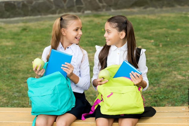 Pause repas au grand air. Des enfants heureux prennent des pommes dans des sacs d'école. Les petites filles profitent des vacances scolaires à l'extérieur. Manger et grignoter sainement. Pause goûter nature. Alimentation et nutrition. Pause pour le déjeuner.