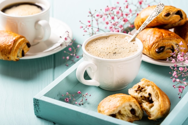 Pause de vacances avec tasse de café, mini pain au chocolat croissants frais et fleurs d'oeillet sur surface turquoise