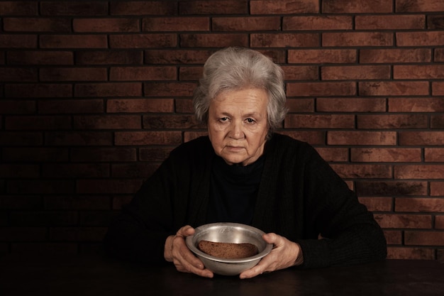 Pauvre femme mûre avec du pain et un bol à table