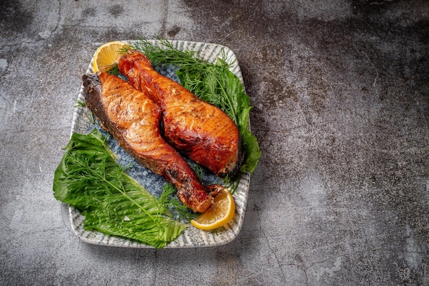 Pavé de saumon au four avec citron, salade et vert d'aneth et de persil sur une assiette contre une table en pierre grise