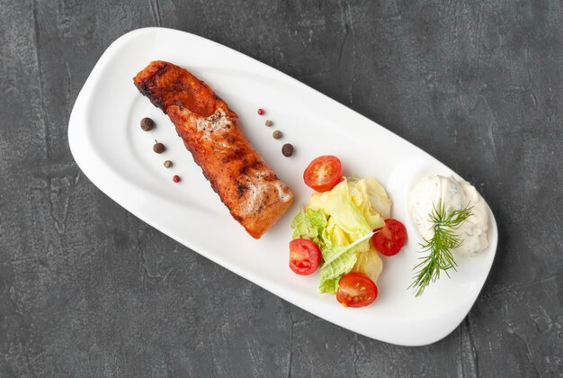 Pavé de saumon aux légumes frais et sauce tzatziki. Sur une assiette blanche. Vue d'en-haut. Sur un fond de béton gris.