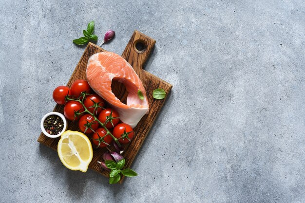 Pavé de saumon cru avec légumes, myrtilles et noix sur une planche de bois sur fond de béton. Vitamines. Alimentation biologique. Livraison de nourriture.