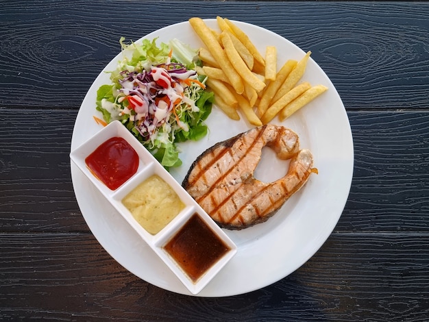 Pavé de saumon grillé avec salade trois sauces et frites sur fond de bois