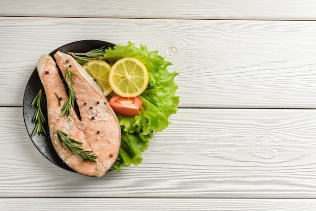 Pavé de saumon prêt avec laitue, citron et tomate sur un mur de table en bois avec espace de copie.