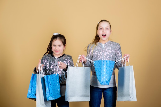 Payez moins Filles soeurs amies avec des sacs à provisions fond beige Shopping et achat Vendredi noir Vente et remise Journée shopping Les enfants tiennent des paquets de bouquets Mode pour enfants Attendez-vous à plus