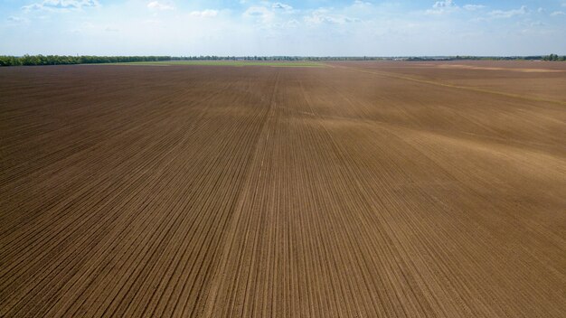 Paysage agricole, champ labouré au printemps et forêt au loin contre le ciel bleu, préparation de la terre pour les travaux de semis. Photo du drone