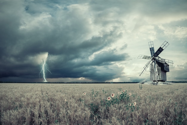 Paysage agricole vintage avec champs de blé et moulin à vent vintage, foudre et orage. Filtre à film