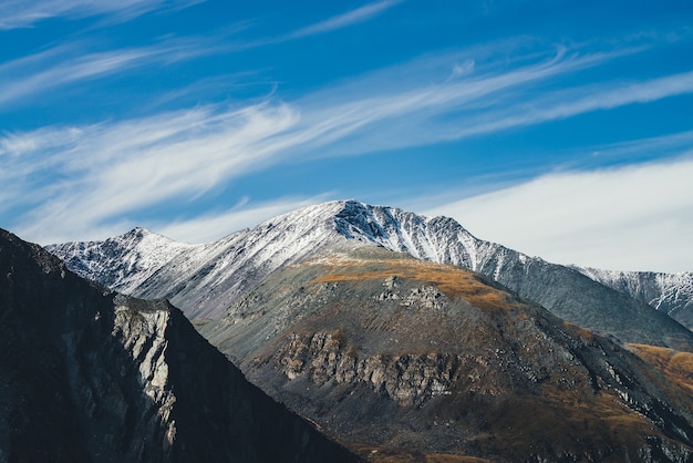 Paysage alpin coloré avec une grande montagne aux couleurs d'automne avec de la neige au sommet du soleil sous les cirrus dans le ciel bleu. Paysage d'automne pittoresque avec des rochers ensoleillés et le sommet d'une montagne enneigée