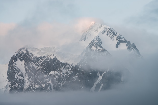 Paysage alpin pittoresque avec des montagnes enneigées à l'intérieur de nuages bas au lever du soleil. Beau glacier dans un brouillard dense. Douce lumière du matin à travers les nuages. Paysage fantomatique avec des Rocheuses dans un ciel nuageux dans des tons pastel