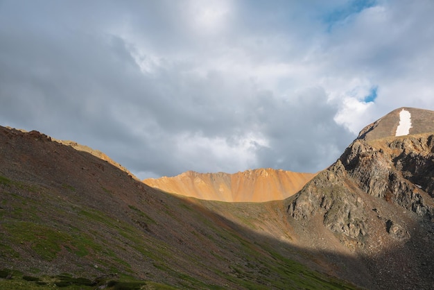 Paysage alpin spectaculaire avec une large crête de montagne éclairée par le soleil sous un ciel couvert par temps changeant Paysage de montagne atmosphérique avec de gros rochers pointus au sommet de la crête à la lumière du soleil sous un ciel nuageux