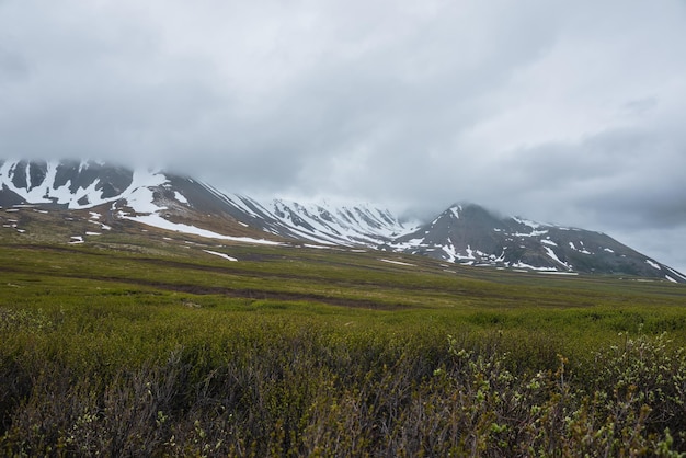 Paysage alpin spectaculaire avec des montagnes enneigées dans des nuages bas gris Paysage atmosphérique sombre de la toundra sous un ciel gris plomb Sombre vue minimaliste sur la chaîne de montagnes parmi les nuages bas pluvieux dans le ciel couvert