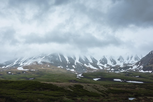 Photo paysage alpin spectaculaire avec des montagnes enneigées dans des nuages bas gris paysage atmosphérique sombre de la toundra sous un ciel gris plomb sombre vue minimaliste sur la chaîne de montagnes parmi les nuages bas pluvieux dans le ciel couvert