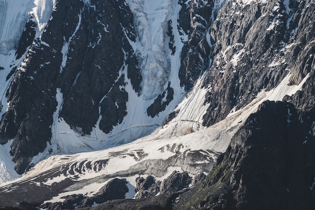 Paysage alpin texturé minimaliste atmosphérique de montagnes rocheuses enneigées avec langue de glacier. flanc de montagne enneigé. Des fissures sur la glace sur une pente raide. Paysages majestueux en haute altitude.