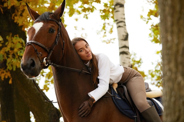 Paysage d'automne belle fille brune aux cheveux longs posant avec un cheval rouge dans la forêt