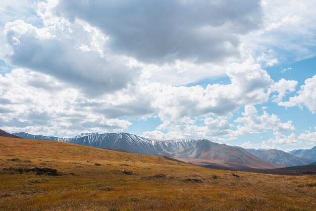 Paysage d'automne hétéroclite avec des collines sur un haut plateau et une chaîne de montagnes enneigées ensoleillées sous un ciel nuageux spectaculaire Couleurs d'automne vives dans les montagnes Lumière du soleil et ombres des nuages par temps changeant