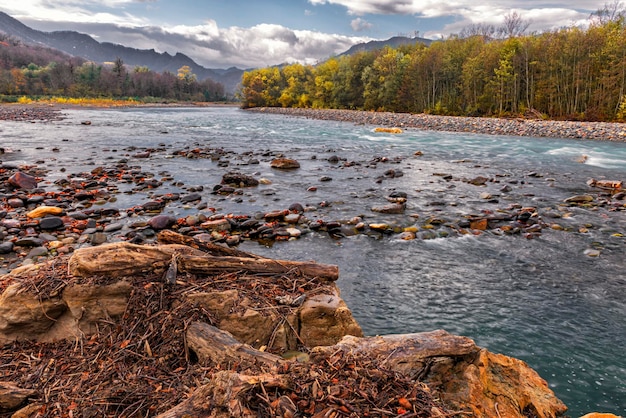 Paysage d'automne d'une rivière de montagne boisée avec un éclairage inégal des nuages