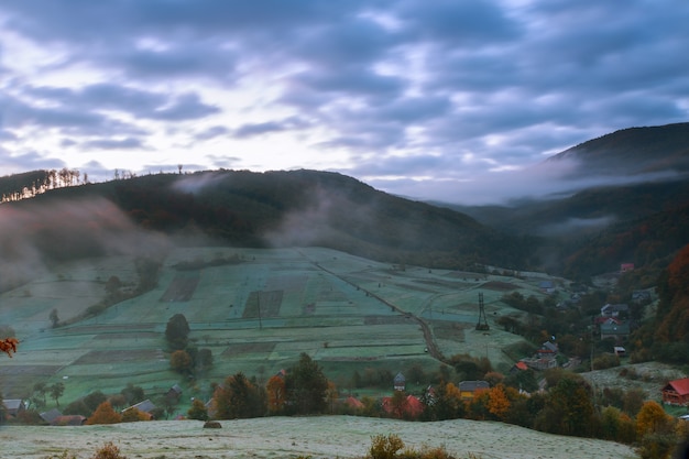 Paysage d&#39;automne. village à flanc de colline. forêt dans le brouillard sur les montagnes à la nuit de pleine lune