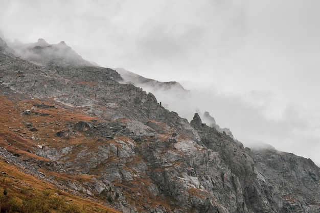 Paysage brumeux atmosphérique avec des silhouettes floues de roches pointues dans des nuages bas pendant la pluie Vue spectaculaire sur de grandes montagnes floues dans la brume de pluie dans des nuages bas gris