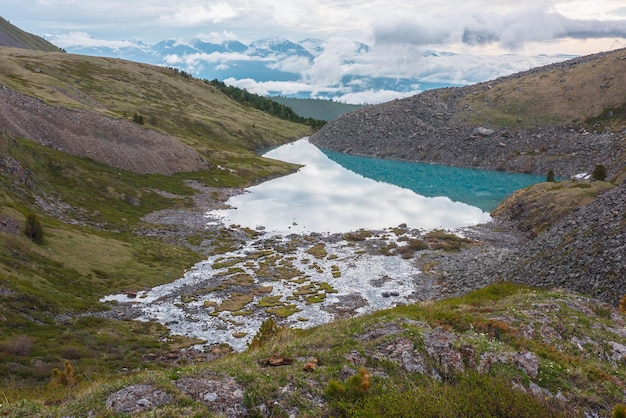 Paysage coloré avec lac de montagne azur avec réflexion du ciel nuageux contre la haute chaîne de montagnes enneigées dans les nuages bas Vue panoramique sur le lac bleu dans la vallée verte et les grandes montagnes enneigées dans les nuages bas