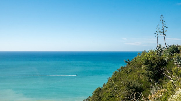 Paysage côtier simple avec un bateau qui passe en arrière-plan créant une piste de bateau