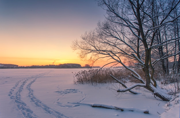 Paysage du lac couvert de glace en hiver avec les empreintes de pas de personnes dans la neige au coucher du soleil